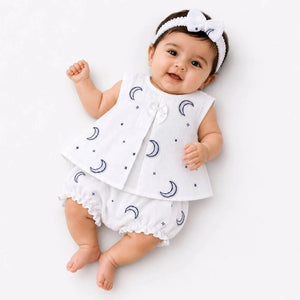 Baby girl wearing white muslin frock, matching bloomer and hairband with blue moon print