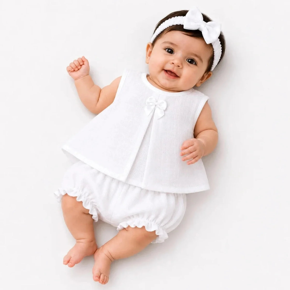 Baby girl wearing plain white muslin frock, matching bloomer and hairband
