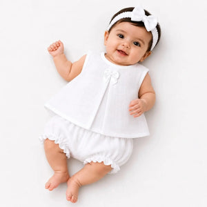 Baby girl wearing plain white muslin frock, matching bloomer and hairband