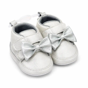 Metallic silver baby girl first walker shoes with decorative bow, hook and loop strap and soft sole – angled view