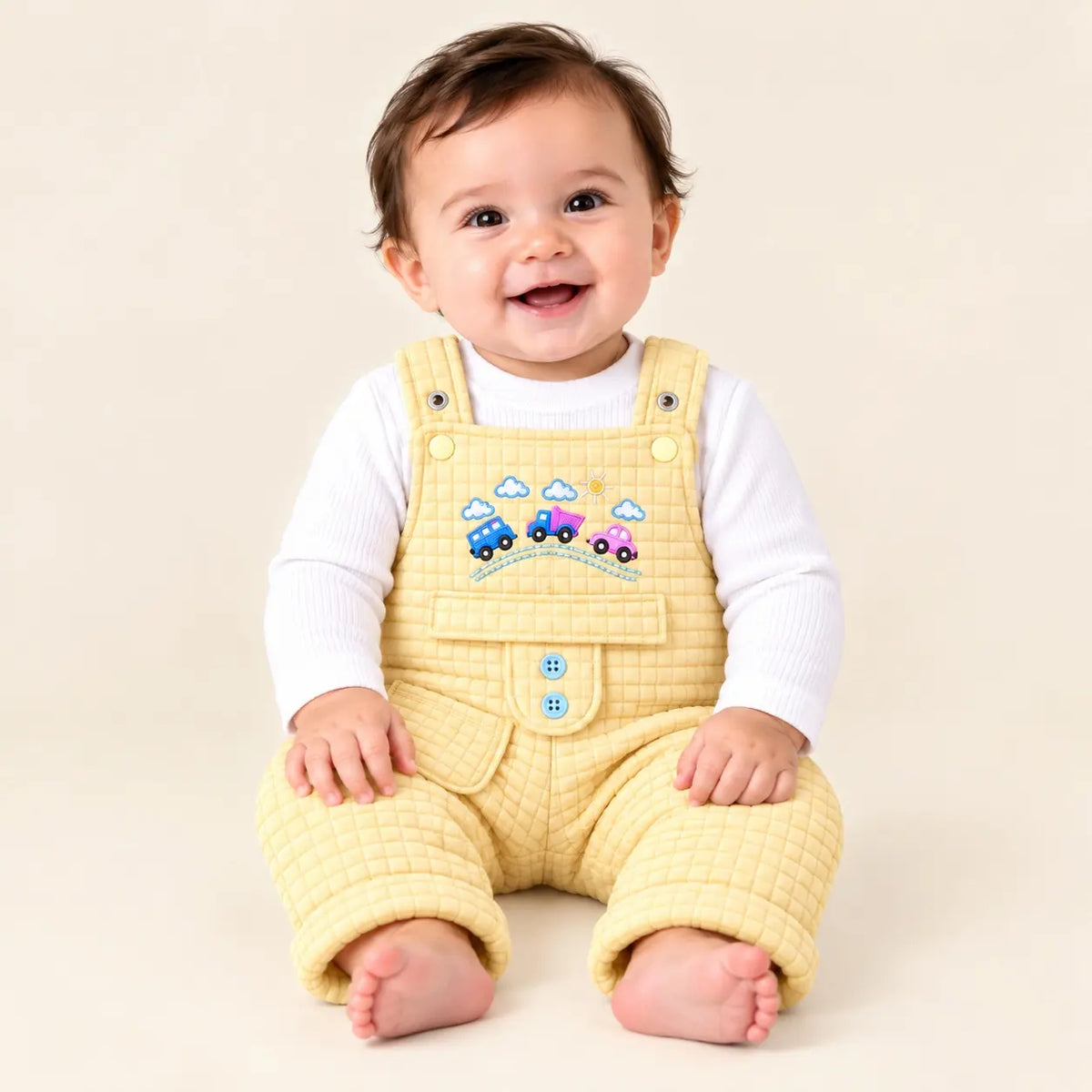 Smiling baby wearing light yellow quilted dungaree romper with white ribbed inner shirt and colorful embroidered cars