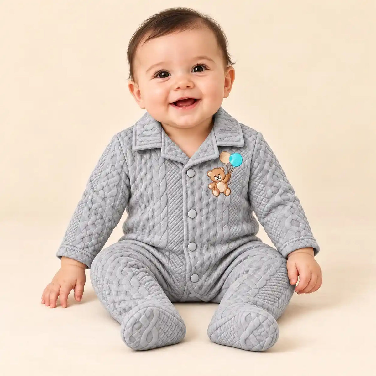 Baby wearing light grey winter quilted footed romper with teddy bear embroidery and textured cable-style pattern in seated pose