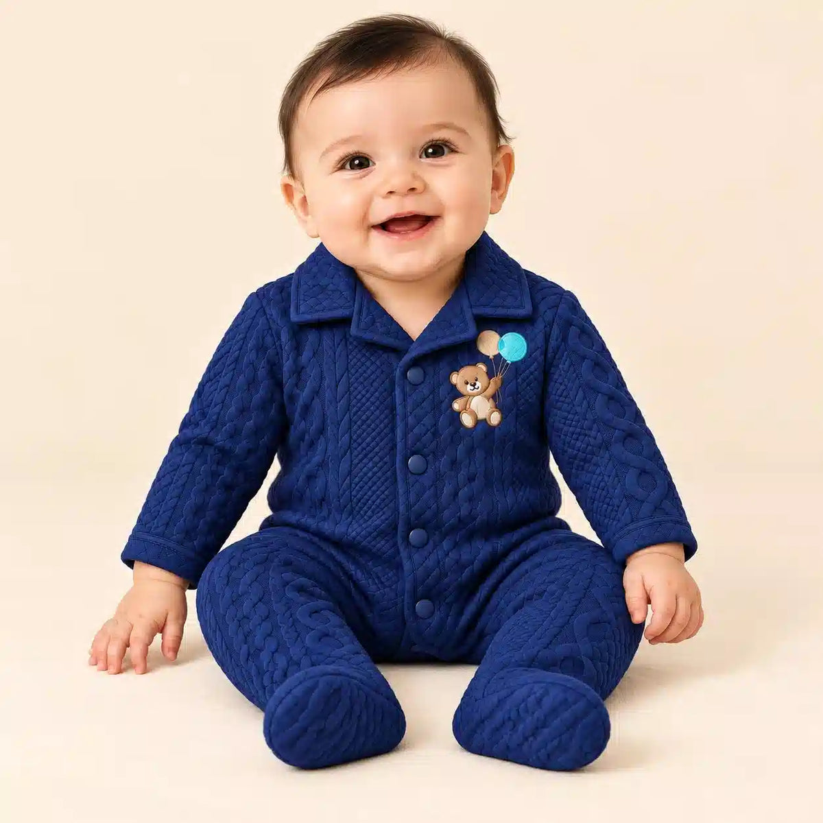 Baby wearing navy blue winter quilted footed romper with teddy bear embroidery in seated pose