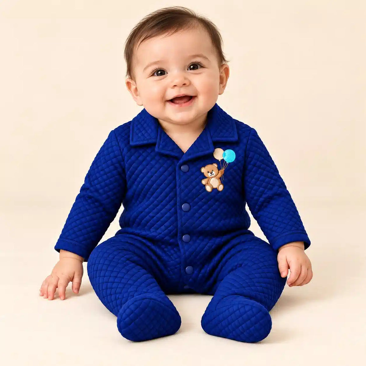 Baby wearing royal blue diamond quilted winter footed romper with teddy bear embroidery in seated pose
