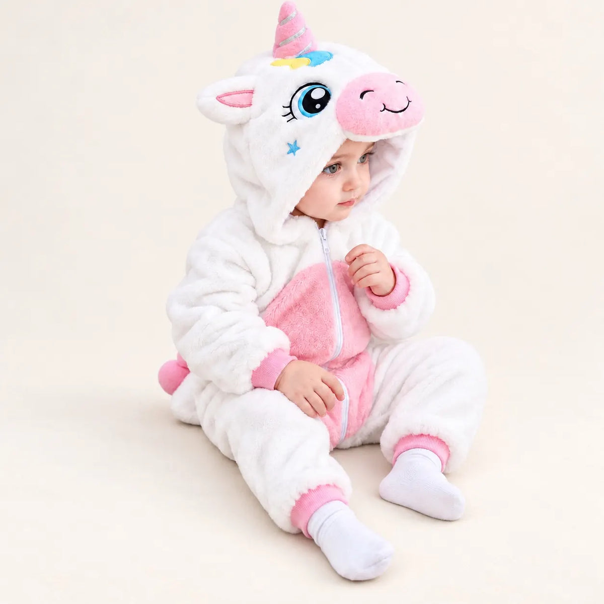 Child sitting in white and pink Unicorn Fleece Costume Jumpsuit with smiling unicorn hood, soft pink belly panel and ribbed ankle cuffs