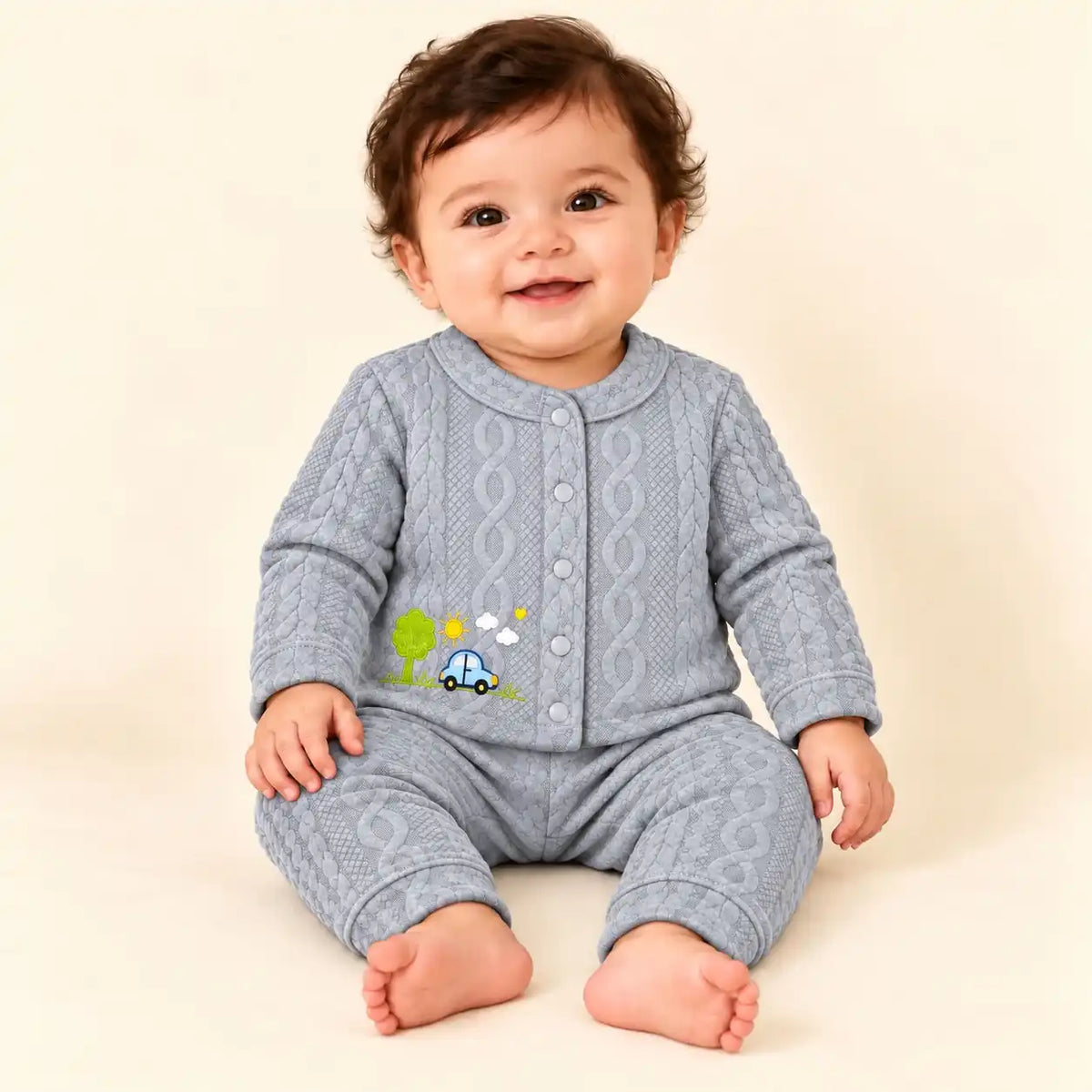 Baby wearing light grey winter shirt and pajama set with blue car, green tree and sunshine embroidery