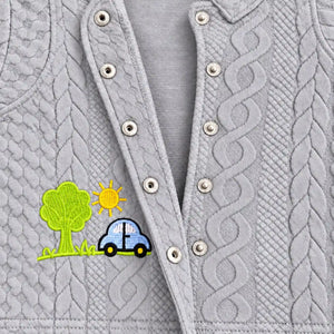 Close-up of open metal snap buttons, raised cable-style texture and car embroidery on light grey baby shirt