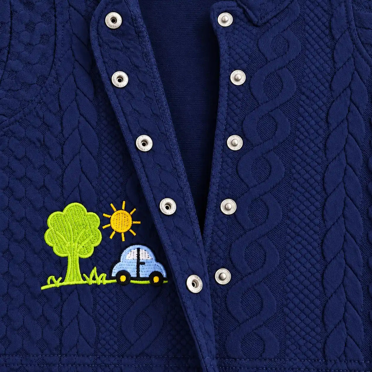 Close-up of open metal snap buttons and car and tree embroidery on navy blue textured baby shirt