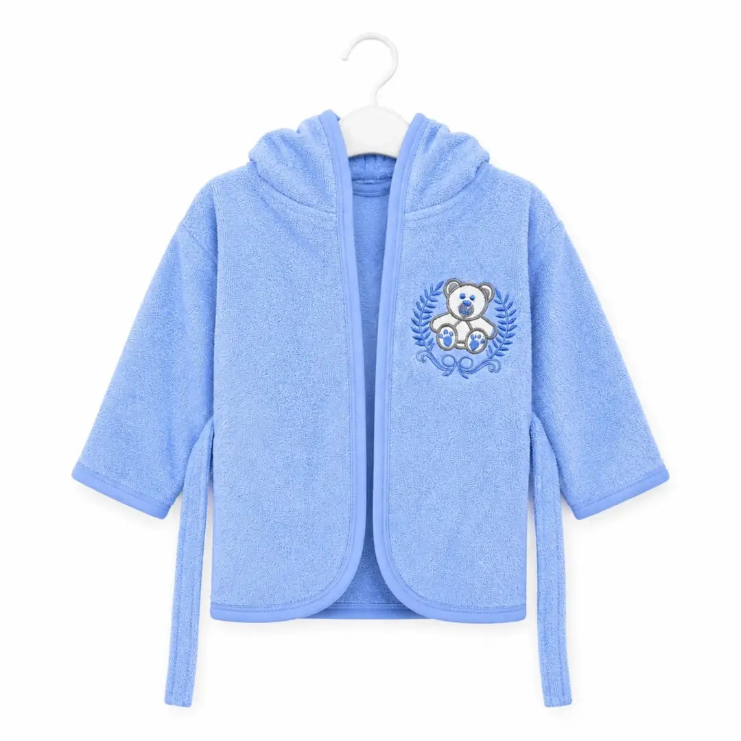 Baby wearing blue hooded bathrobe with teddy bear embroidery on white background