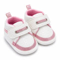 White textured baby shoes with pink glitter accents and strap closure angled view